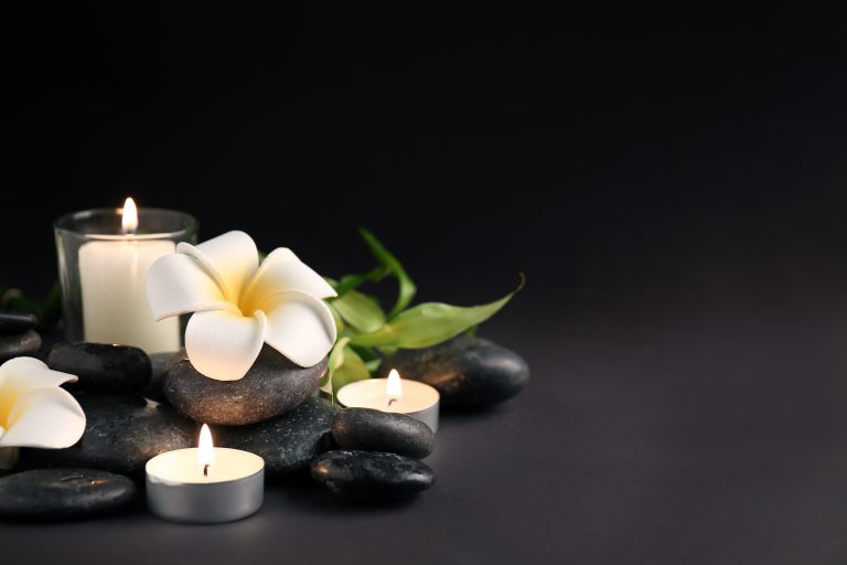 white flower with tea lights and black rocks on a dark background