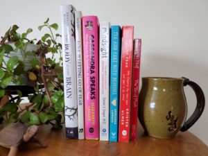 Books upright between a mug and a plant